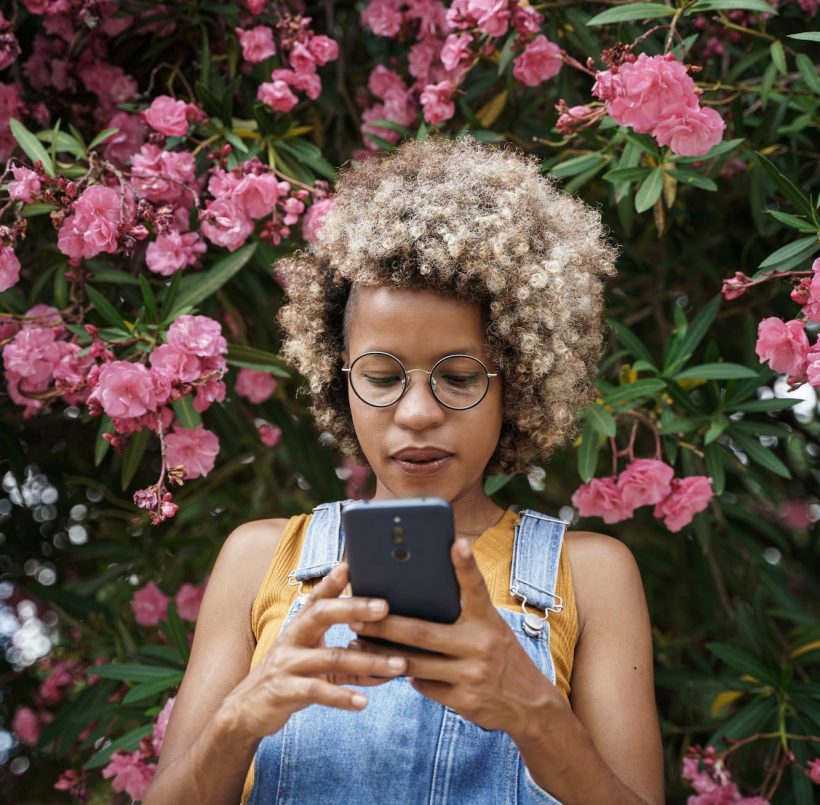 Cool young modern black woman with blond hair using smart phone for social media